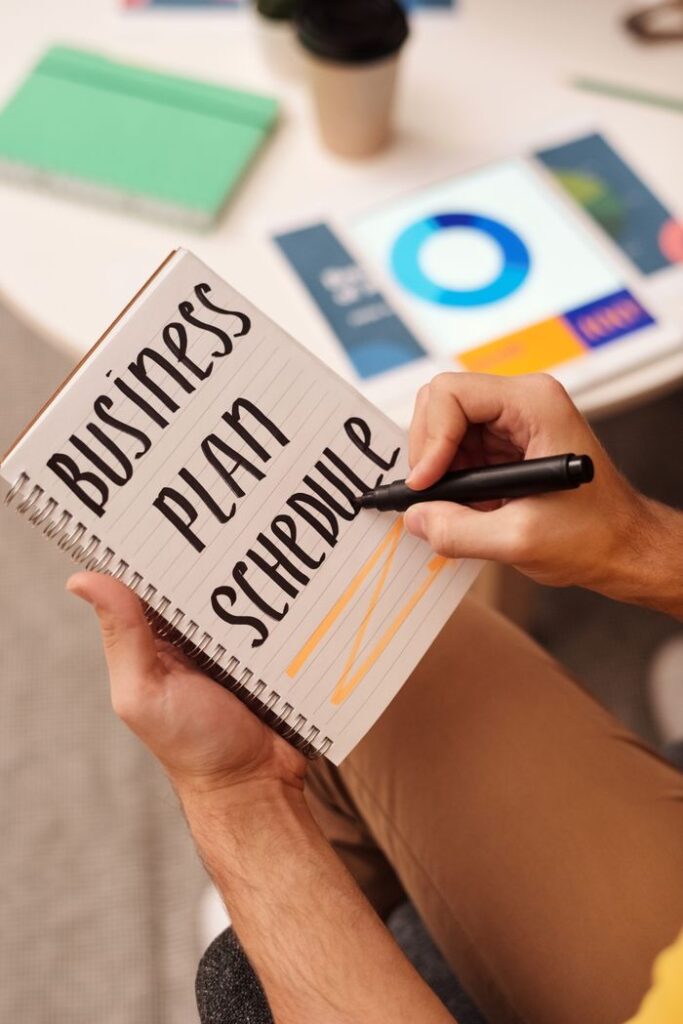Close-up of hands writing 'Business Plan Schedule' in a notebook during a meeting.